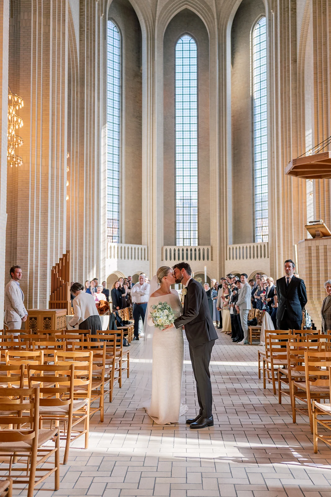 A wedding ceremony in a bright room with tall arched windows