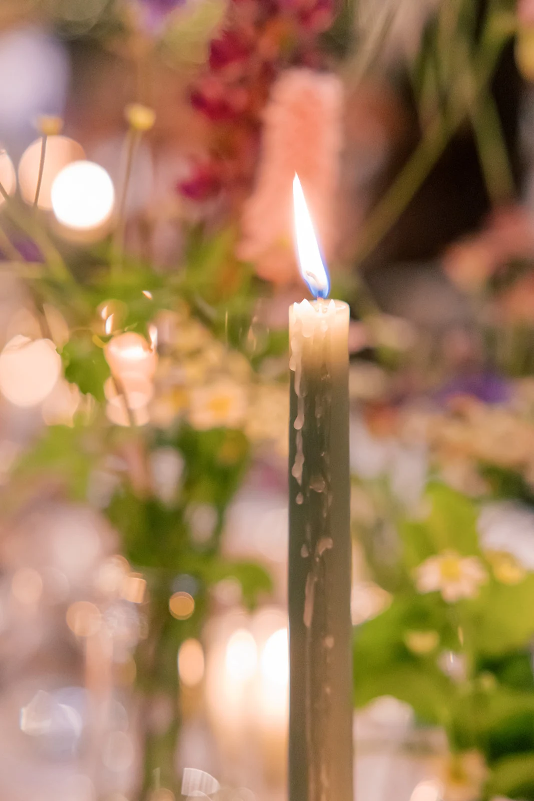 A lit green taper candle at a wedding reception