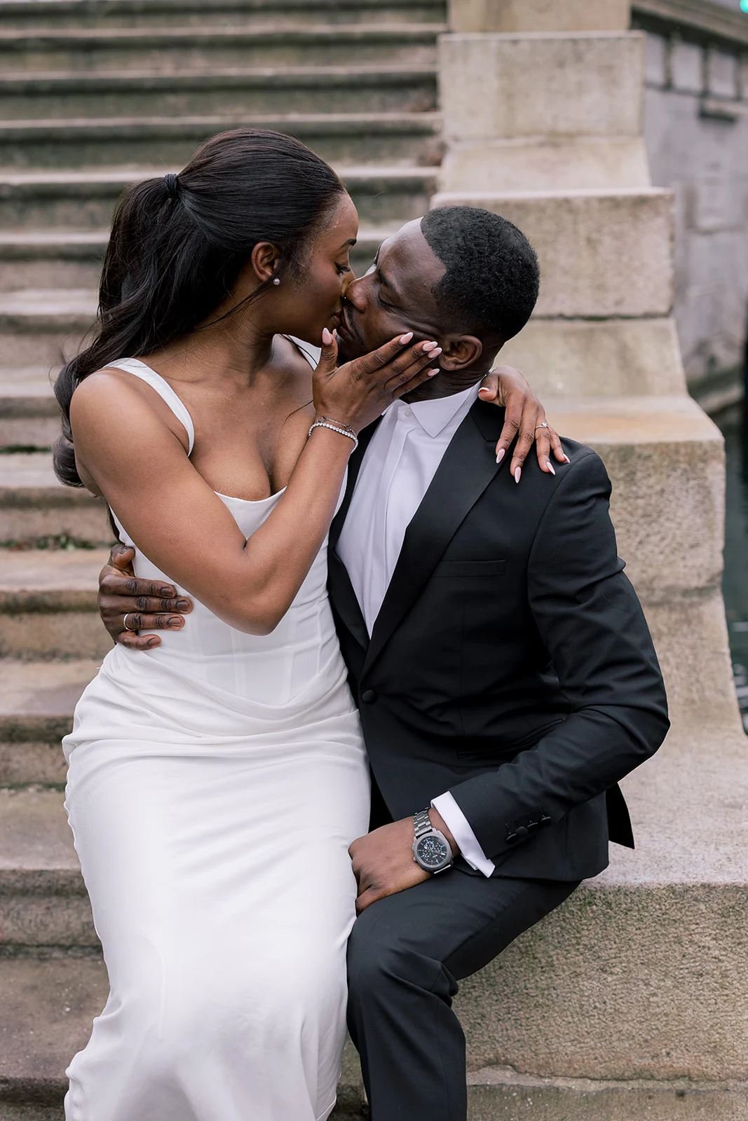 Newlyweds sharing a kiss while seated on stone steps