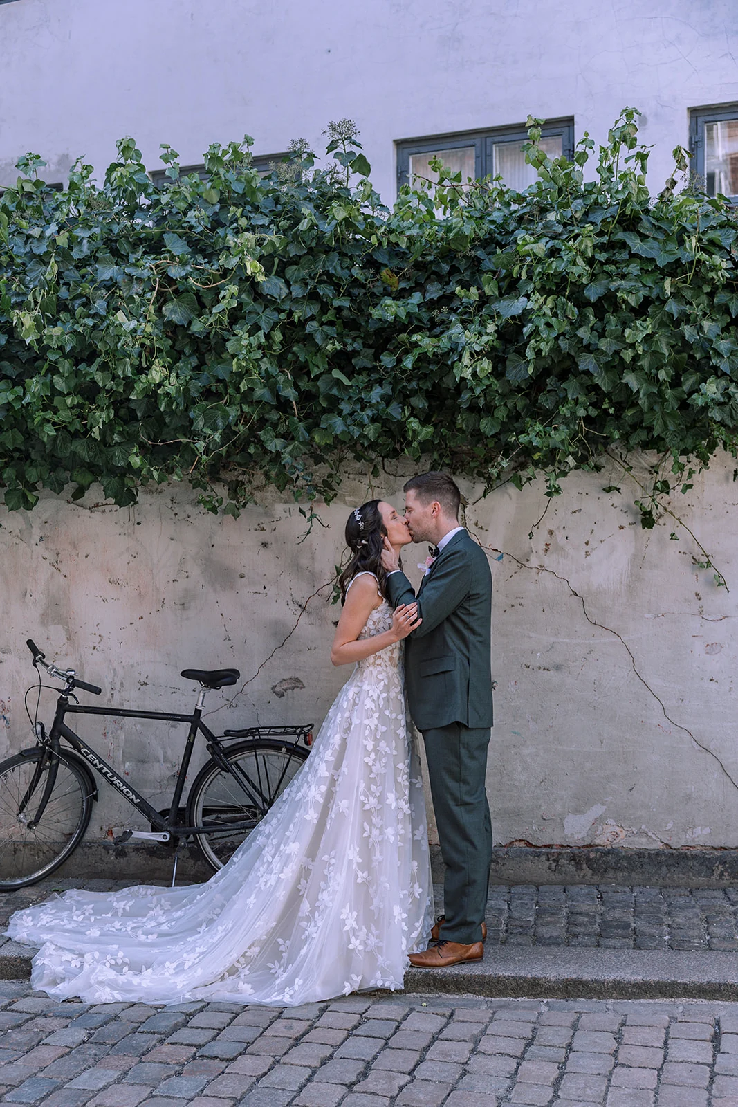 A wedding couple kissing beside ivy and a bicycle on a cobbled street