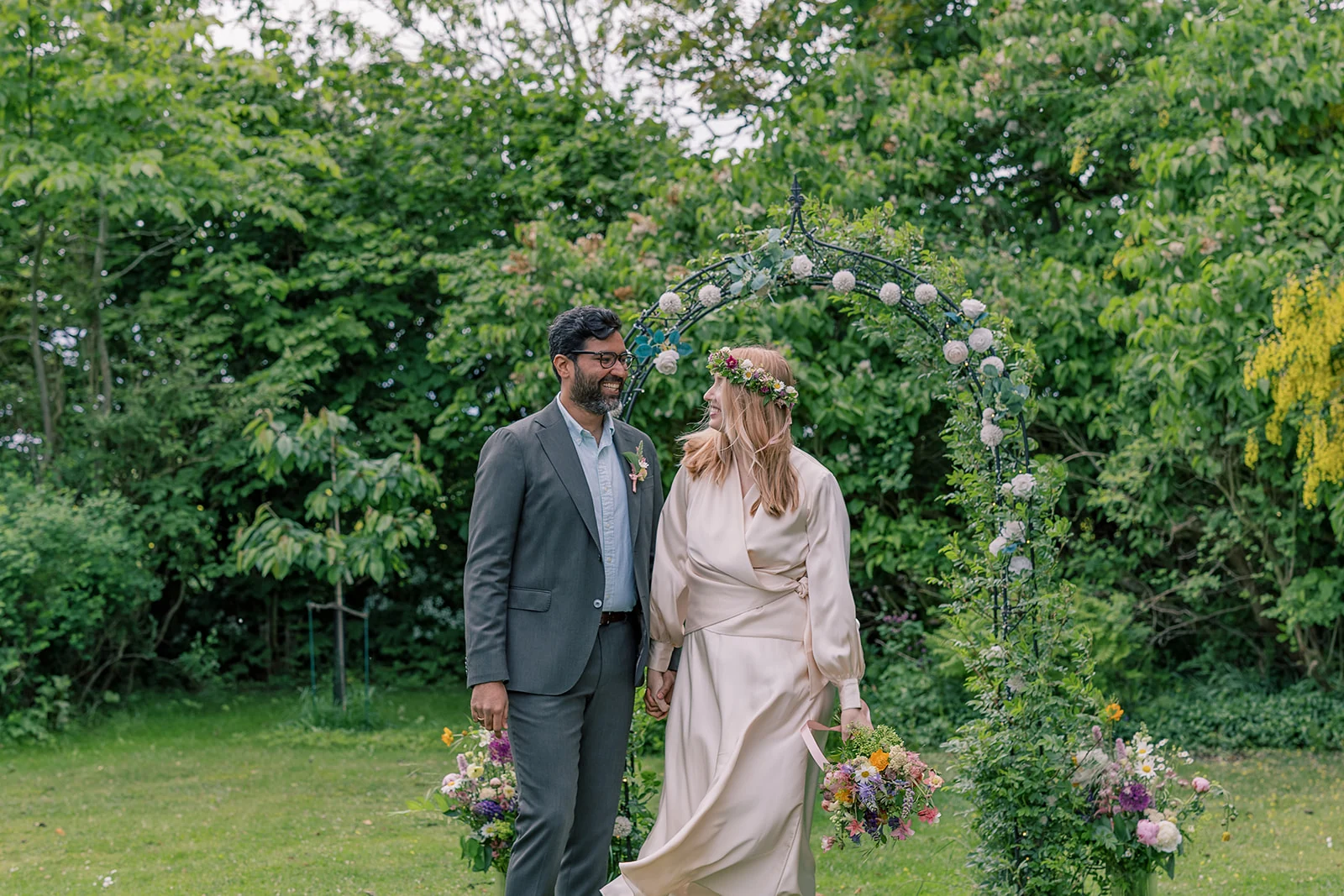 A wedding couple walking together beneath a leafy arch