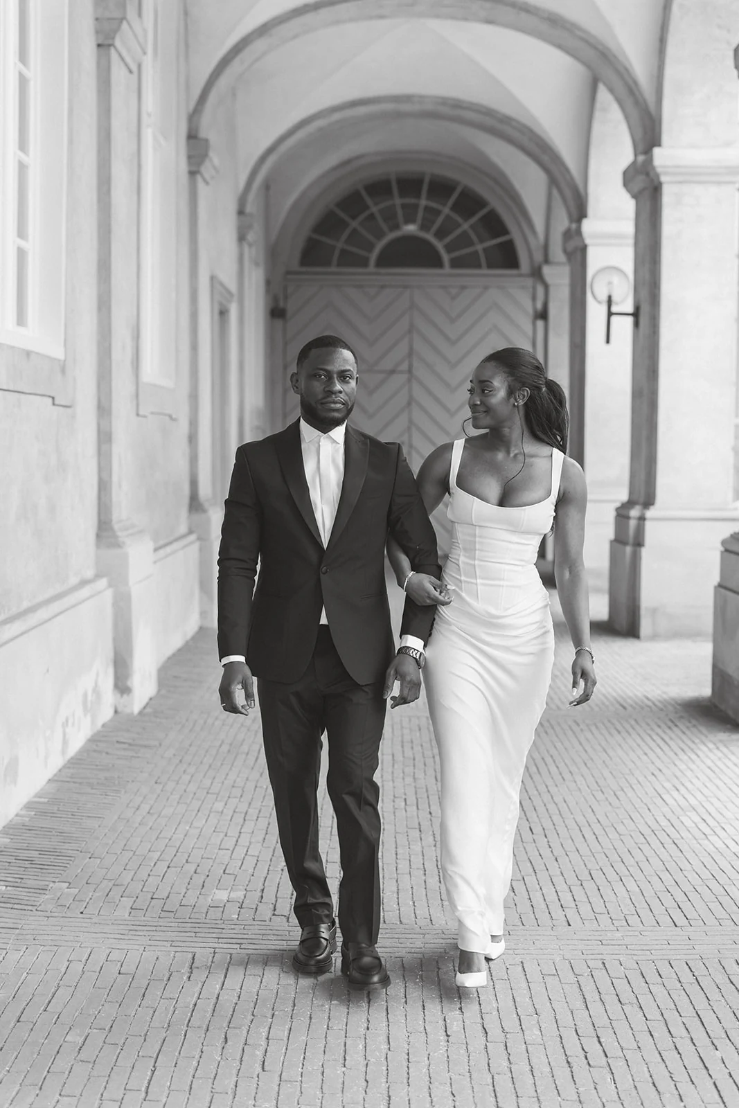 Newlyweds walking through a vaulted stone hallway, in black and white