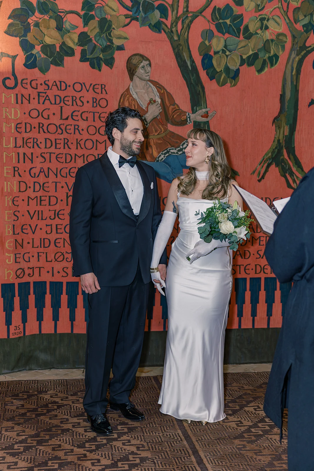 Newlyweds together in a room with richly colored tapestries