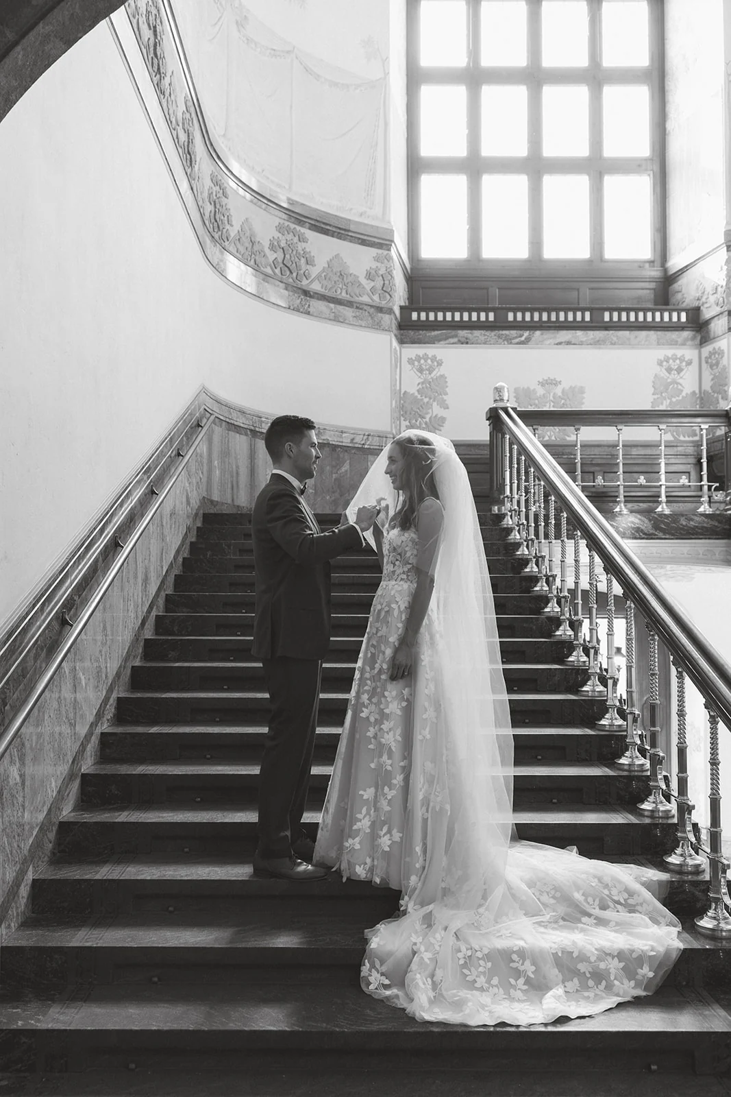 Newlyweds together on a sweeping staircase, photographed in black and white
