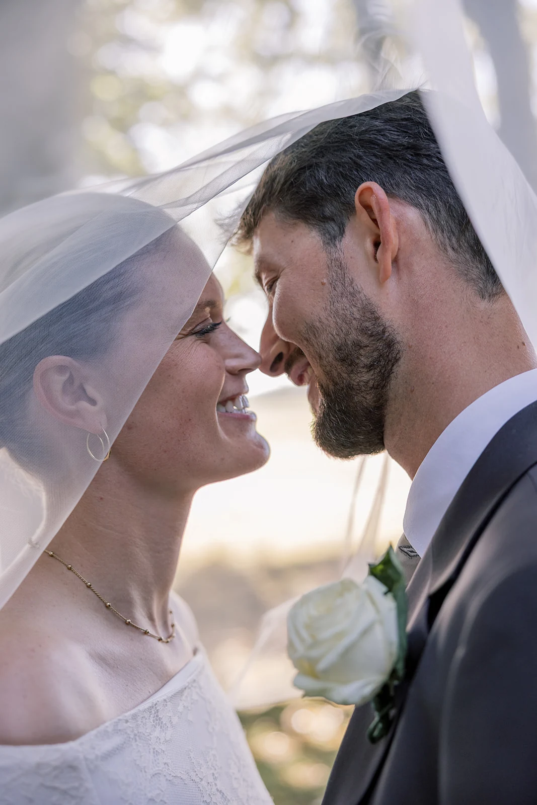A bride and groom smiling beneath a veil