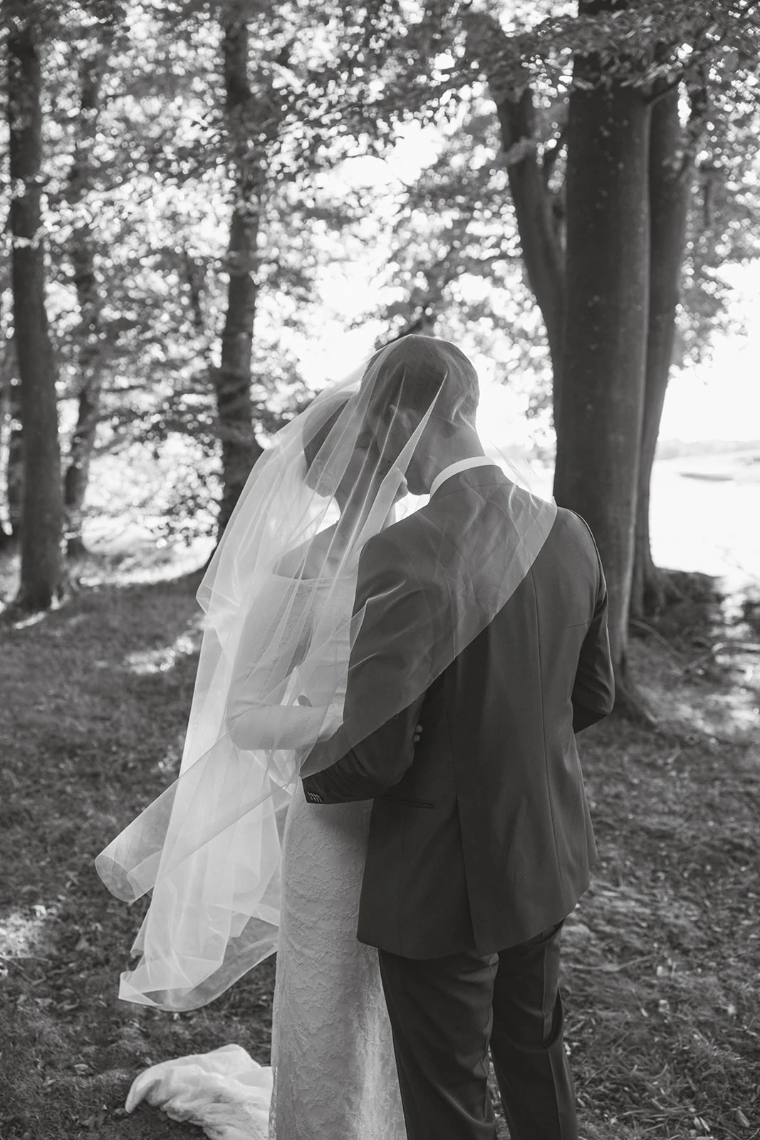 A couple beneath a veil in a wooded garden, in black and white